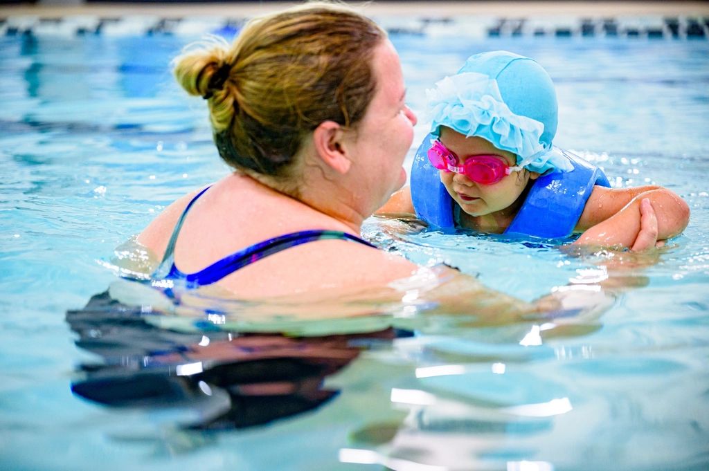Instructora enseñando a nadar a una niña con lentes y gorro